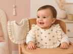 Bébé portant un bavoir à cœurs avec le second bavoir uni du lot